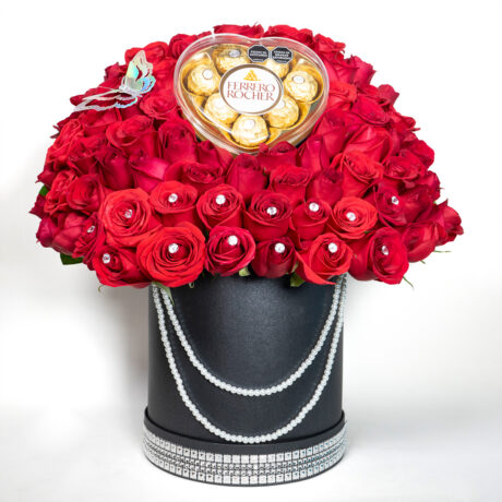 caja de muchas rosas rojas con base tambor negro y una mariposa plateada en la paete superior y chocolates ferrero rocher y cinta de diamantes en la parte inferior