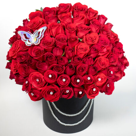 caja de muchas rosas rojas con base tambor negro y una mariposa plateada en la paete superior