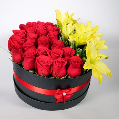 caja de flores, rosas y lirios tambor negro y moño rojo