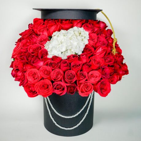 caja de muchas rosas rojas y hortensias con base tambor negro y gorro de grado